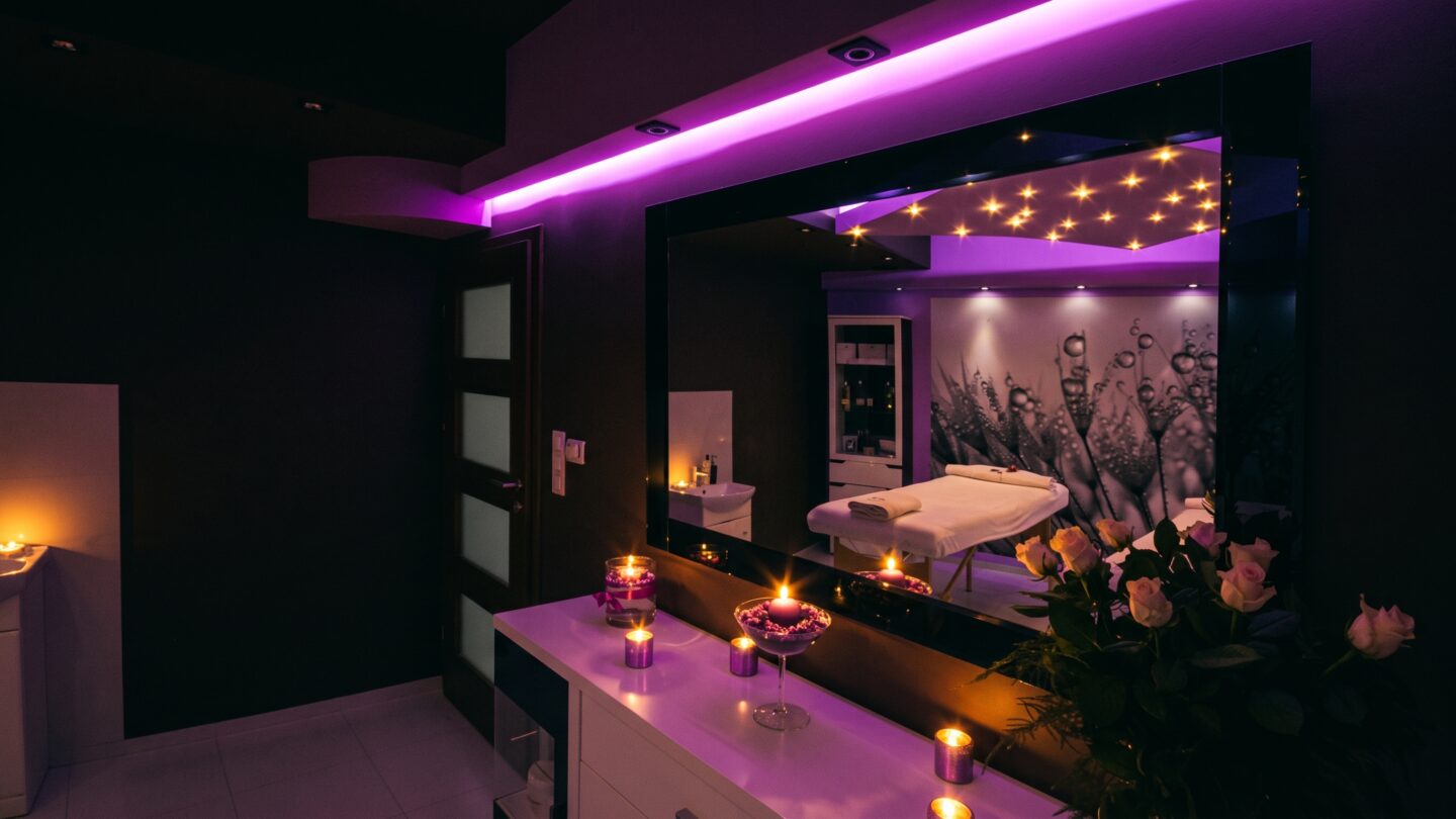 Intérieur d'un salon de massage bien-être avec table de soin, ambiance tamisée, éclairage LED violet et bougies